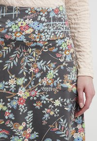 Sukně se vzorem květin v šedé barvě, zdobená vícebarevnými květy, listy a motivy ptáků. Vyrobena z měkké látky s přiléhavým pasem.