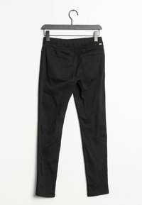Un pantalon stretch noir suspendu sur un cintre noir. Il présente une texture lisse, deux poches arrière et une coupe ajustée.