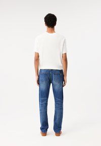 T-shirt bianco a maniche corte abbinato a jeans in denim blu. I jeans presentano un taglio classico con tasche posteriori e un lavaggio scolorito.