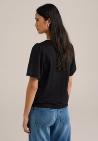 Črn kratkotrajni top s našitimi rokavi, izdelan iz lahkega blaga. Kombiniran z visokim pasom, svetlo modrimi jeans hlačami.