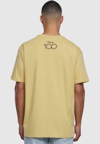 Gul bomull t-skjorte med rund hals og korte ermer. Rygdesignen har "Disney 100" i svart. Myk tekstur og avslappet passform.