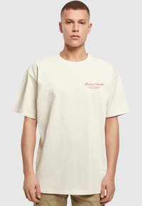 Cream-colored cotton t-shirt with short sleeves, a relaxed fit, and pink text reading "Italian Cuisine" on the front. Minimalist design.