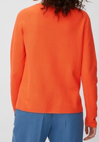 Pull-over en tricot orange avec une finition texturée, présentant un col rond et des manches longues, associé à un pantalon bleu clair.