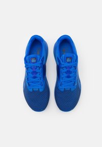 Blå sportskor med ovandel i mesh, platta snören och vadderad krage. Har en texturerad sula och märkesdetaljer på sidan.