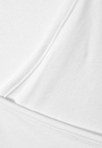Primo piano di un tessuto bianco, che mette in risalto la consistenza morbida, la superficie liscia e le linee pulite con un sottile dettaglio di cucitura, riflettendo un design minimalista.