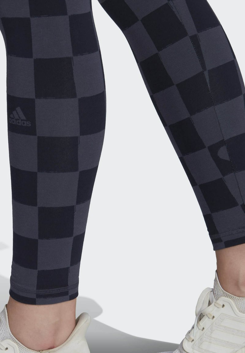 Schwarz-graue karierte Leggings mit weicher Textur, featuring ein Adidas-Logo an dem linken Bein. Abgerundeter Saum am Knöchel, enganliegendes Design.