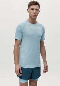 Světle modré sportovní tričko s krátkými rukávy a kulatým výstřihem. Vyznačuje se texturovanou tkaninou a štíhlým střihem, kombinované s tmavě modrými šortkami.