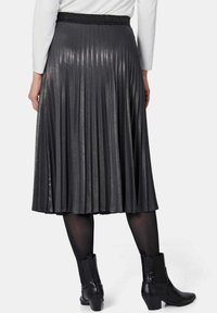 Grijze geplooide rok met een glanzende textuur, voorzien van een brede elastische tailleband. Zwarte enkellaarsjes met een gestructureerd ontwerp complementeren de outfit.
