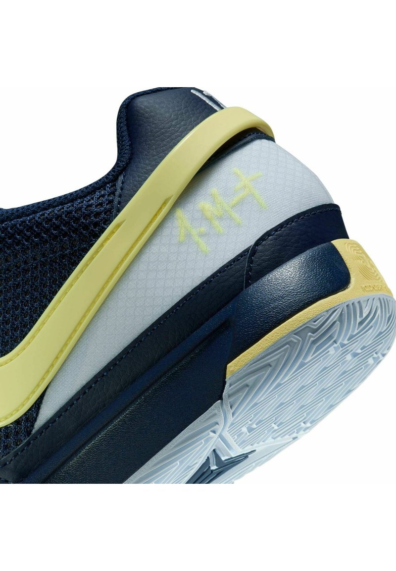 Granatowe buty sportowe z siateczkową cholewką, żółtymi detalami, teksturowaną podeszwą środkową oraz skomplikowanym wzorem z białej gumy na podeszwie.