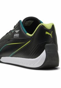 Svart atletisk sko med texturerad yta, gröna och teal detaljer, vit sula, med en häl som liknar kolfiber och logodetaljer.