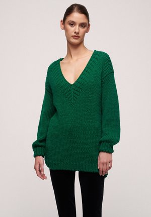 Green knitted sweater with a deep V-neck, textured ribbing, and wide sleeves. Made of chunky yarn, featuring a relaxed fit.