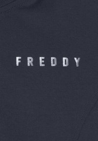 Tessuto blu navy scuro con la parola "FREDDY" in argento metallico, posizionata centralmente, su uno sfondo di tessuto liscio e testurizzato.
