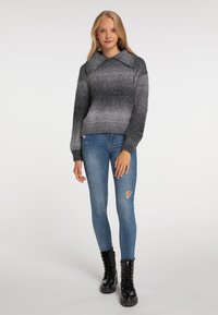 Grijze ombre trui met een kraaghalslijn, gecombineerd met strakke blauwe jeans met een versleten knie, en zwarte veterschoenen tot de enkel.