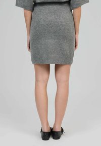 Robe pull en maille grise avec une silhouette ajustée, ourlet côtelé et texture douce. Portée avec des chaussures noires, vue de dos.