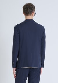 Giacca da abito blu navy con vestibilità su misura, due spacchi posteriori e polsini a quattro bottoni. Realizzata in tessuto liscio, con dettagli di design minimalisti.