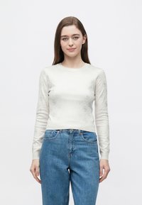 Maglione a maniche lunghe color crema con motivo a cerchi piccoli in rilievo, silhouette aderente e polsini a coste. Abbinato a jeans blu.