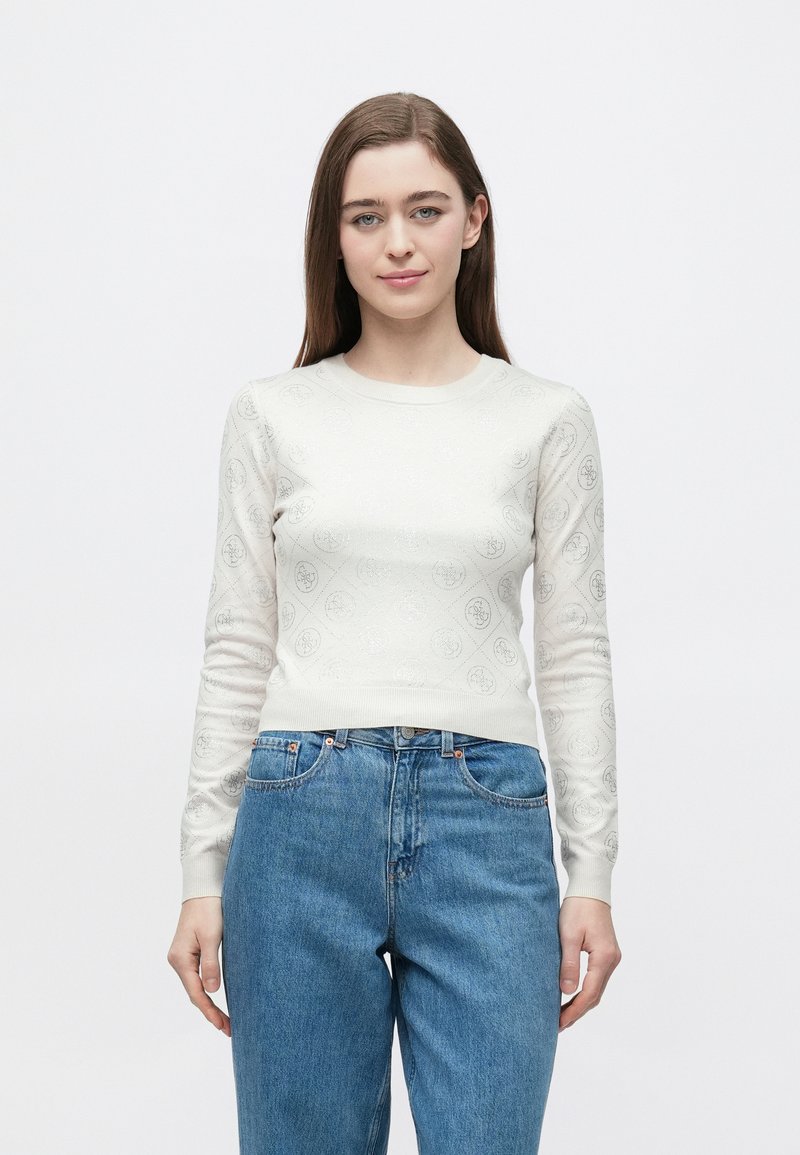 Maglione a maniche lunghe color crema con motivo a cerchi piccoli in rilievo, silhouette aderente e polsini a coste. Abbinato a jeans blu.