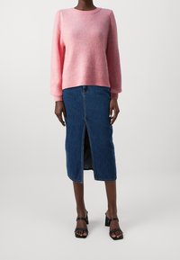 Růžový žebrovaný svetr s dlouhými rukávy, spárovaný s džínovou midi sukní s předním rozparkem. Černé sandály na blokovém podpatku doplňují celý outfit.