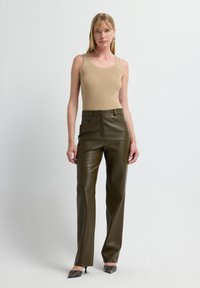 Beige gerippter Tank-Top kombiniert mit hochtaillierten, glänzenden olivgrünen Kunstlederhosen. Die Hosen verfügen über Seitentaschen und einen vorderen Knopfverschluss.