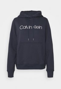 Námořnická modrá mikina s kapucí, s tkaničkou kolem kapuce, velkou přední kapsou a bílým logem "Calvin Klein" přes hruď. Směs bavlny.