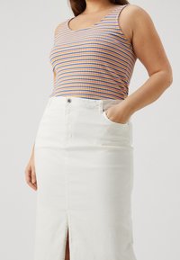 Top sin mangas a rayas en naranja, azul y púrpura con un diseño ajustado, combinado con una falda de mezclilla blanca con una abertura frontal y bolsillos.