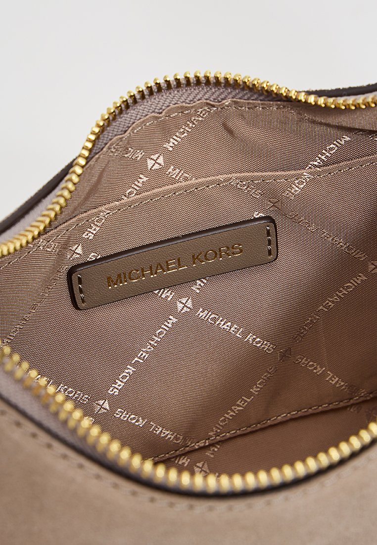 Bruine binnenkant van een tas met een gouden ritssluiting, met een stoffen voering met herhalende logo's en een leren label met de tekst "Michael Kors" in reliëf.