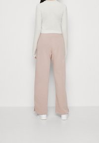 Ljust rosa vida joggers i mjukt material, med slitsar i fållarna, tillsammans med en figurnära vit långärmad tröja. Vita sneakers synliga.