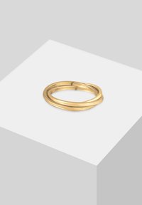 Divi savstarpēji savīti gludi zelta gredzeni atrodas uz baltas virsmas ar gaiši pelēku fonu.