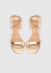 Gold metallic high-heeled sandals with a square toe, two wide straps across the front, and a wraparound ankle strap. Smooth texture.