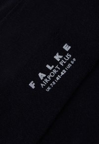 Calcetín negro con textura suave, que presenta el logo impreso en blanco "FALKE AIRPORT PLUS" y detalles de tamaño en el costado.