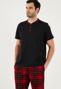 Zwarte kortemouwen shirt met een kraag in rood ruitpatroon en vier knopen, gecombineerd met rode ruitbroek met zwarte en witte lijnen.