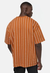 Brunstripete oversized t-skjorte med hvite vertikale striper, laget av bomull, med korte ermer og en avslappet passform, sett fra baksiden.