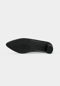 Semelle de chaussure noire à bout pointu avec motif floral décoratif et petit talon bloc, vue de dessous sur fond blanc.