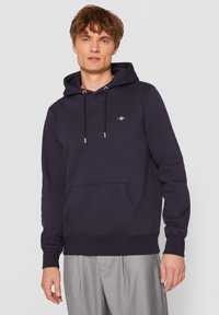 Sweat à capuche bleu marine foncé en tissu doux, avec une poche avant, une capuche à cordon de serrage et un discret logo sur la poitrine.