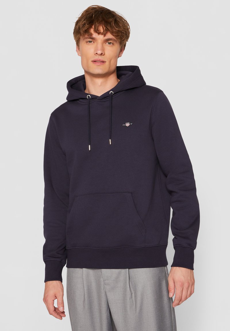 Sweat à capuche bleu marine foncé en tissu doux, avec une poche avant, une capuche à cordon de serrage et un discret logo sur la poitrine.