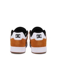 Brown suede and white leather sneakers featuring black accents, a padded collar, and a prominent logo on the back heel. Rubber sole.