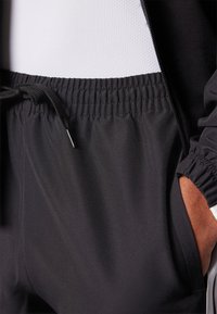 Μαύροι αθλητικοί τζόγκες με ελαστική μέση, λεπτομέρεια κορδονιού και πλαινές τσέπες. Λείος υφή με εφαρμοστό σχέδιο.