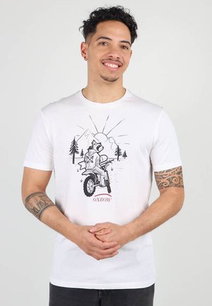 T-shirt en coton blanc avec un imprimé graphique d'un raton laveur chevauchant une moto, agrémenté d'éléments de montagne et de forêt, avec le texte "OXBOW" en dessous.