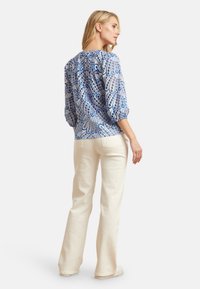 Blauw en wit gemusterde top met puffmouwen, gecombineerd met lichtbeige broeken. De stof lijkt lichtgewicht met een zachte textuur.