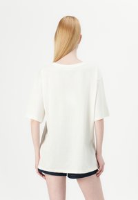 T-shirt en coton blanc surdimensionné à manches courtes et col rond, associé à des shorts en denim foncé. Design minimaliste, sans motifs.