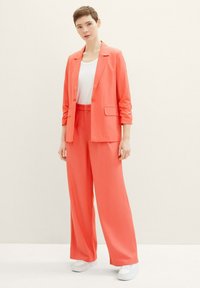 Coral blazer and wide-leg pants set. Blazer features notch lapels and a single button. White undershirt and white sneakers complete the look.