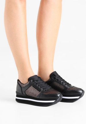 Baskets à plateforme noires avec panneaux en mesh portées pieds nus sur fond blanc, vues de face et de profil.