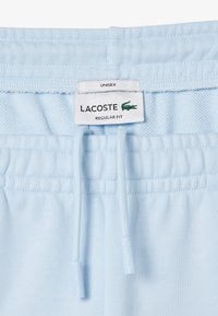 Shorts unisex azzurri chiari con vita elasticizzata, dotati di un laccetto con punte brandizzate. Include un'etichetta con la scritta "LACOSTE REGULAR FIT."