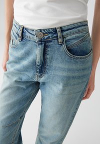 Lichtblauwe denimspijkerbroek met een hoge tailleband, voorzien van een metalen knoopsluiting, vijf zakken en subtiele vervaging langs de benen.