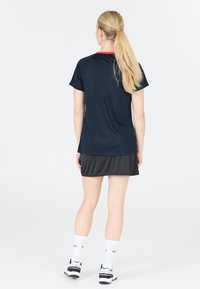 Marineblå atletisk T-shirt med rød krave, parret med en sort nederdel. Stoffet ser let og glat ud, egnet til sportsaktiviteter.