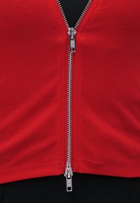 Silberner Doppelschieber-Reißverschluss auf geripptem rotem Stoff vor schwarzem Kleidungsstück-Hintergrund.