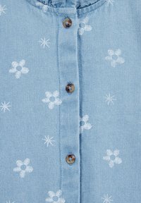Világoskék ing farmer anyagból, fehér virág- és csillagmintákkal, kerek nyakkivágással és barna gombokkal az elején.
