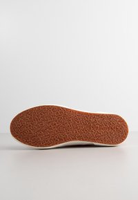 Podeszwa buta z teksturowym, brązowym bieżnikiem z nieregularnymi wzorami oraz nazwą marki "Superga" wytłoczoną w okolicy pięty.