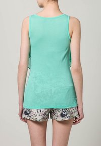 Top senza maniche di colore verde menta realizzato in tessuto morbido, caratterizzato da una vestibilità comoda. Il modello indossa pantaloni corti con stampe floreali, visibili nella parte inferiore.