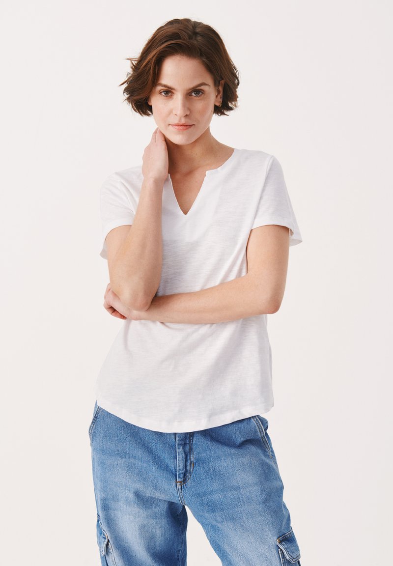 T-shirt bianco a maniche corte con scollatura a V e una texture sottile, abbinato a pantaloni cargo in denim blu con tasche e una vestibilità comoda.